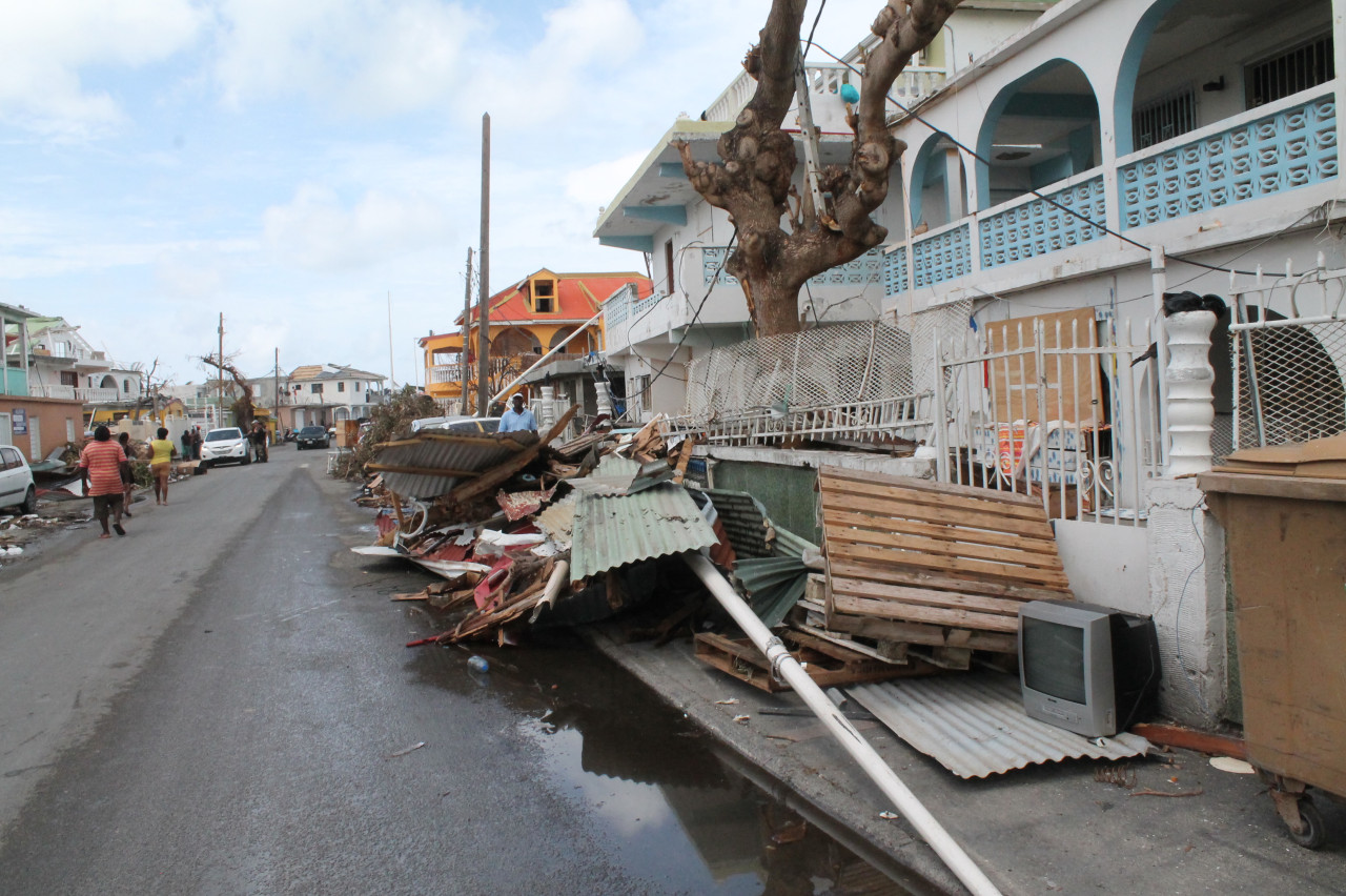 Photo des dégâts causés par le cyclone Irma à Saint-Martin, en 2017. Les rues sont jonchées de débris. Des bâtiments sont endommagés. Et les lignes électriques sont tombées.