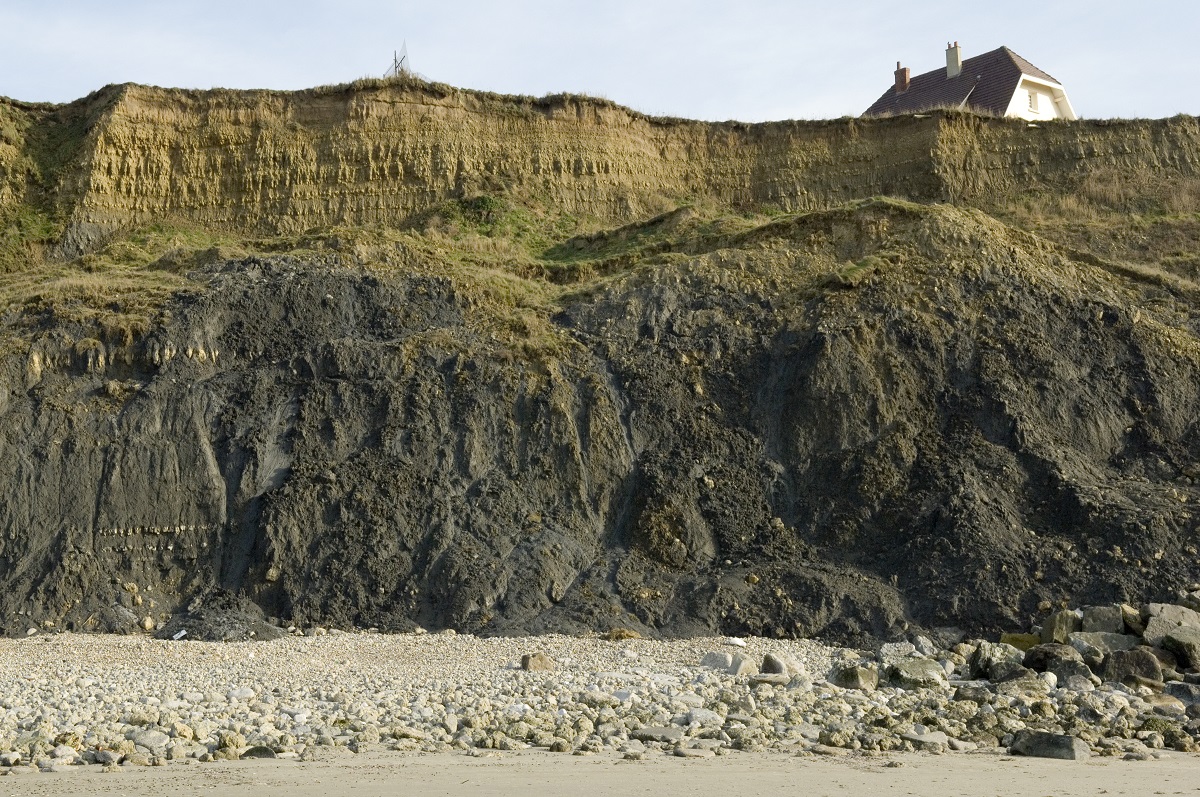 Photo d’une maison en bord de falaise. On y voit clairement l’érosion de la falaise et des éboulements.