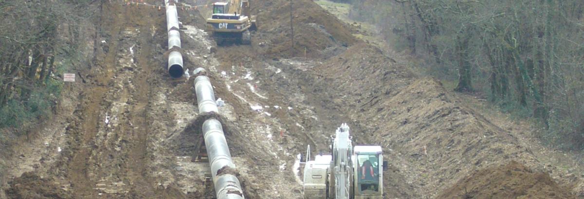 Photo prise sur un chantier d’installation d’une canalisation de transport de matière dangereuse. Une pelleteuse est en train de creuser une tranchée pour un tuyau de très gros diamètre.