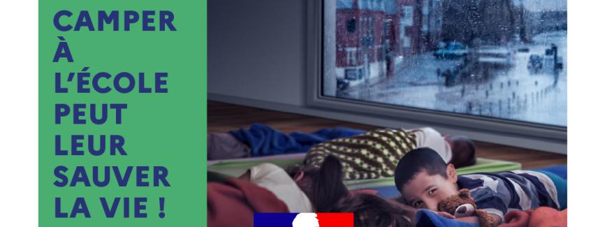 L’une des affiches de la campagne. Des enfants dorment sur des matelas dans une grande salle alors que, par la fenêtre, on voit que c’est le soir et que de fortes précipitations tombent sur la ville.  Le texte : « Camper à l’école peut leur sauver la vie ! »